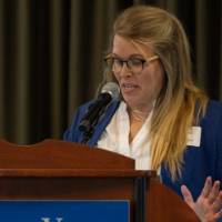 Woman in blue blazer speaks into microphone on podium with the GVSU logo